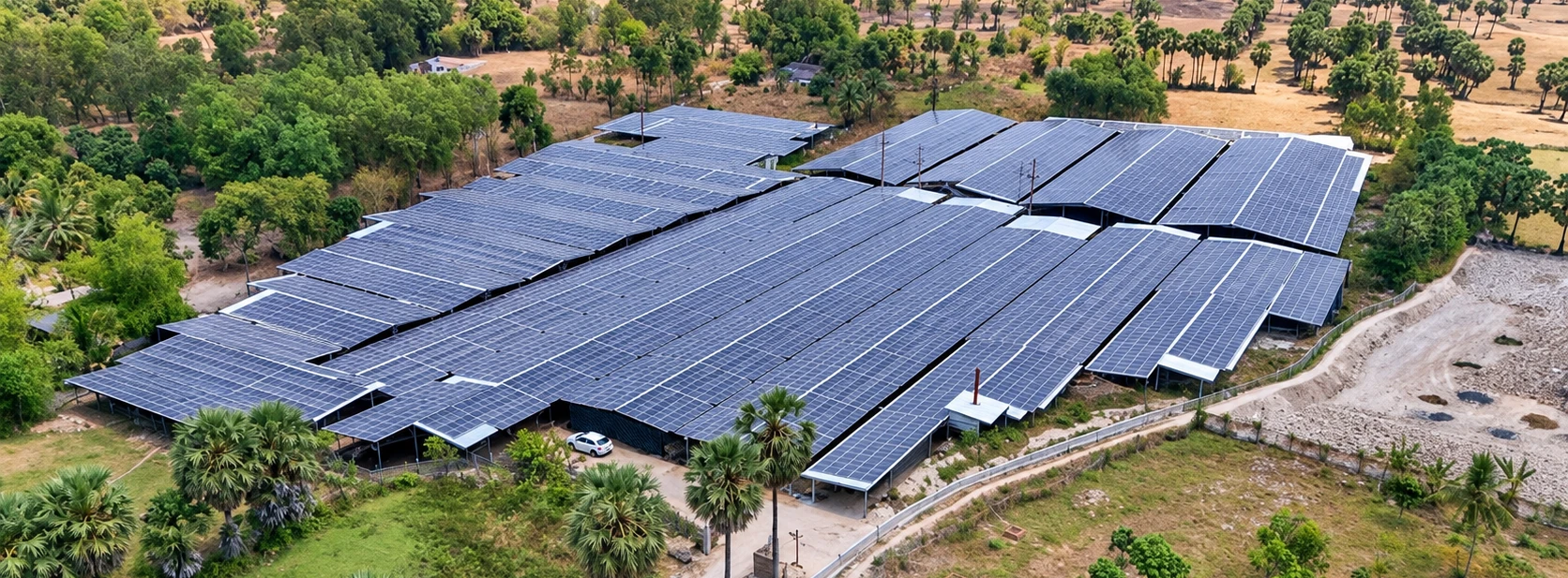 Các dãy nhà mái lợp tấm pin mặt trời giữa cây xanh và hàng thốt nốt, nhìn từ trên cao